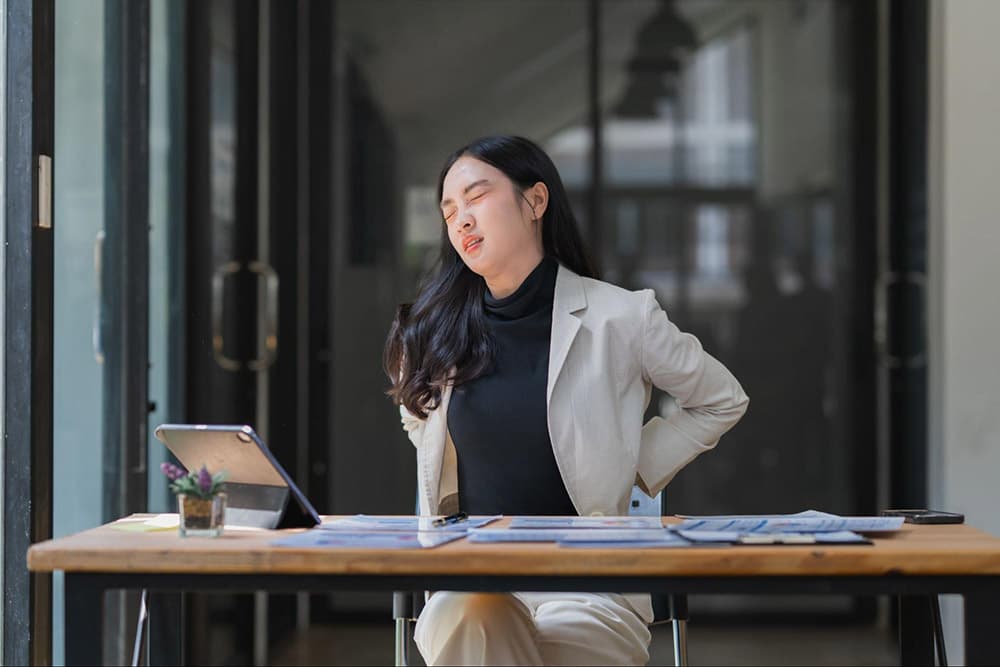Woman experiencing lower back and tailbone pain while sitting at a desk