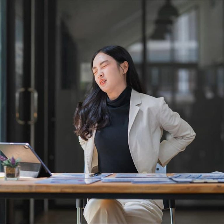 Woman experiencing lower back and tailbone pain while sitting at a desk